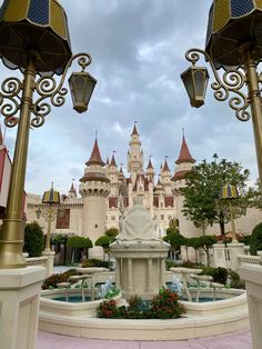 a fountain in front of a castle with two lights on it's sides and flowers around the base