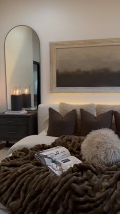 a bed with pillows and blankets on it in front of a large mirror, framed art above the bed