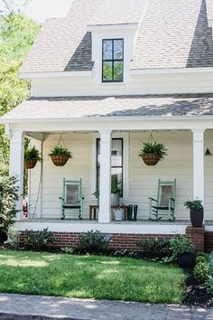 a white house with two rocking chairs on the front porch and potted plants outside