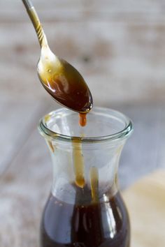 a spoon full of caramel syrup being poured into a glass jar with liquid in it