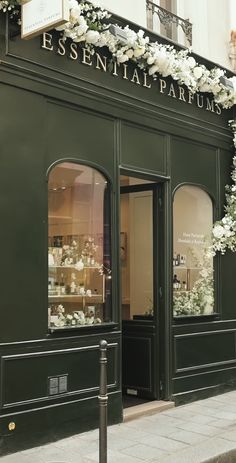 a store front with white flowers on the outside and green doors that say essential parfums