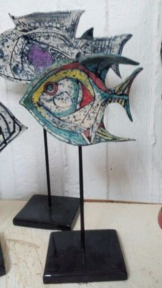 two metal fish sculptures on black stands next to each other and one is painted with different colors