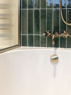 a white bath tub sitting next to a green tiled bathroom wall with gold faucet