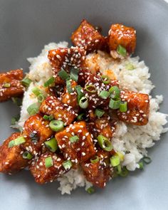 a white plate topped with rice covered in sesame seeds and chicken pieces on top of it