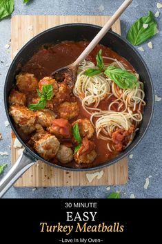 a pan filled with pasta and meatballs on top of a cutting board next to basil leaves