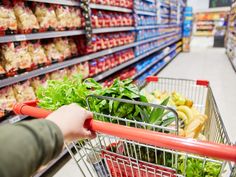 a person pushing a shopping cart through a grocery store filled with fresh vegetables and fruit