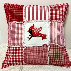 a red and white pillow with a patchwork bird on the front, sitting on a bed