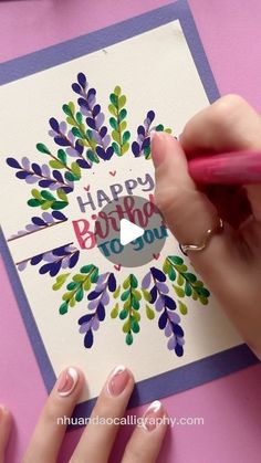 a woman is using a marker to write the words happy birthday on a greeting card