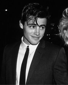 a black and white photo of a young man in a suit smiling at the camera