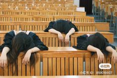 two women are sleeping on wooden benches in a lecture hall, with their heads resting on each other's backs