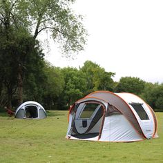 two tents set up in the middle of a field with trees and grass behind them