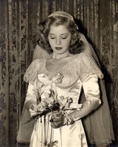 an old black and white photo of a woman in a wedding dress holding a bouquet