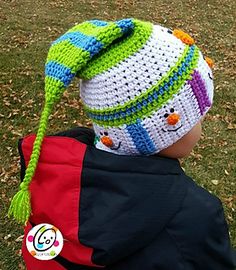 a small child wearing a crocheted hat while sitting in the grass with his back to the camera