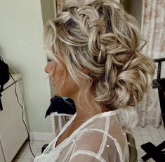 a woman with blonde hair in a braided updo is looking into the mirror