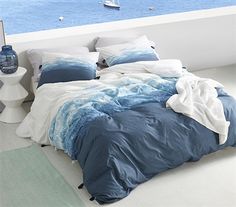 a bed with blue and white comforters in front of a large body of water