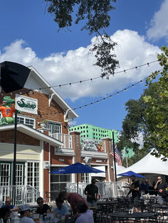 people sitting at tables in front of a building with umbrellas and lights strung from the roof