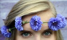 a woman with blue flowers in her hair and eyes looking at the camera while she has long blonde hair