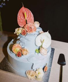 a blue cake with flowers and fruit on the top is sitting on a table next to a knife