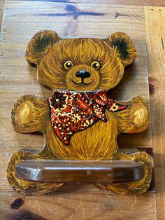 a brown teddy bear sitting on top of a wooden table next to a metal object