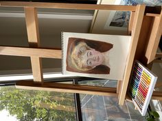 a portrait of a woman is hanging on the wall in front of a window with other pictures