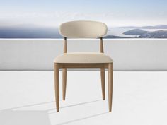 a wooden chair sitting on top of a white floor next to a wall and ocean