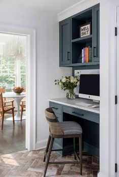 a desk with a computer on top of it in front of a window and some chairs