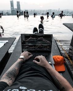 a man sitting in front of a laptop computer on top of a table next to a swimming pool