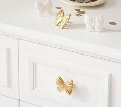 two gold butterflies on top of a white dresser next to some coins and a plate