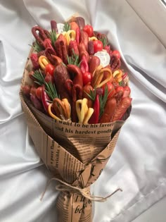 a bouquet of fake vegetables wrapped in brown paper on a white sheeted bed spread