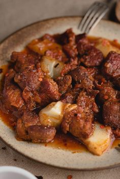 a white plate topped with meat and potatoes covered in gravy next to a fork