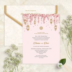 a pink and gold wedding card with flowers on the side, next to some baby's breath