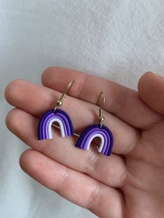 a pair of purple and white earrings in the shape of a rainbow on a person's hand