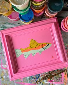 a pink frame with a fish painted on it next to paintbrushes and paints