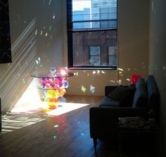 the sun shines brightly on a living room with a glass table and black couch