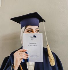 a woman wearing a graduation cap and gown holds up a sheet of paper to her face