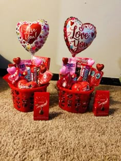 two valentine's day baskets with candy and heart shaped balloons on the floor next to each other