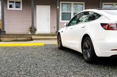 the rear end of a white car parked in front of a house with two windows