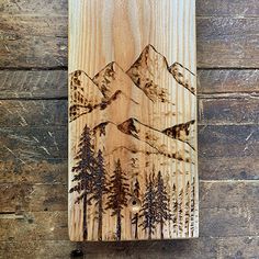 a wooden wall hanging with mountains and trees on the wood paneled wall behind it