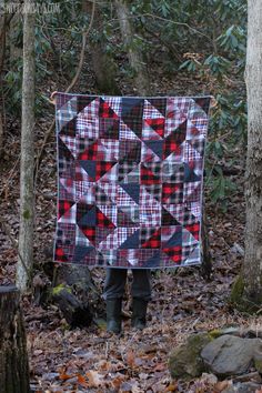 a person standing in the woods holding up a quilt