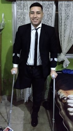 a man in a suit and tie with crutches standing next to a bed