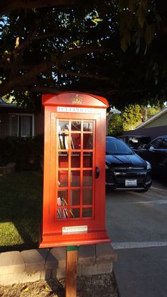 a red phone booth sitting on the side of a road next to a parking lot