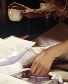 a woman is sitting at a table with papers and a coffee cup in her hand