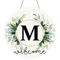 a welcome sign hanging from a rope with the letter m in black and green leaves