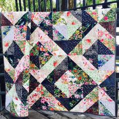 a quilt is hanging on a fence near some trees and bushes, with the background painted in dark blue