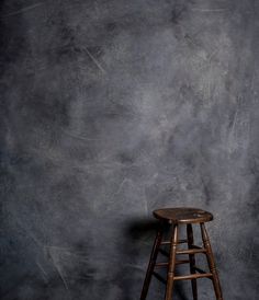 a wooden stool sitting in front of a gray wall