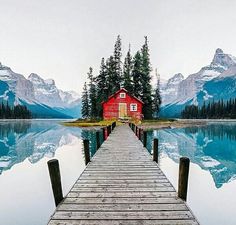 a dock with a red house on it in the middle of mountains and water, surrounded by pine trees