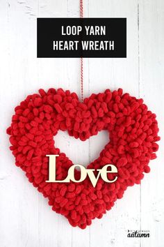 a heart shaped wreath with the word love hanging from it's side on a white wooden background