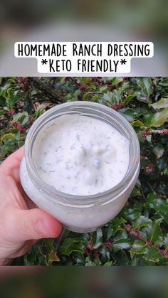 a hand holding a jar of ranch dressing in front of some bushes with the words homemade ranch dressing keto friendly