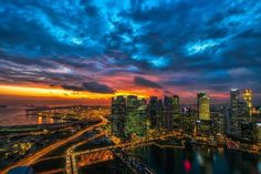 the city skyline is lit up at night with bright lights in the foreground and clouds in the background