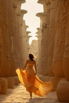 a woman in an orange dress is walking through the egyptian ruins with her long flowing yellow dress